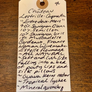 A handwritten wine label tag on a wooden surface, listing Château Lestrille-Capmatin and several Bourgogne wine varietals and descriptors.
