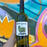 Bottle of wine with a label held in front of a colorful graffiti wall
