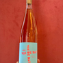 A hand holding a bottle of Rosé Pink wine with a light blue label that reads 'VINE DAYS' in red text, set against a textured red background.