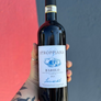 Bottle of Stroppiana Barolo wine held by a person with a tattooed arm against a red and gray background.