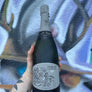 Bottle of champagne held by a person with a tattooed arm on a textured surface