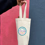 White tote bag with a logo held by a hand on a pink and blue background