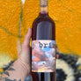 Bottle of j brix wine held by a hand with a colorful background