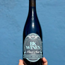 A bottle of BK Wines Carbonic Pinot Noir with a label that includes the brand name and the variety 'Pinot Noir'. The background is blue, and the bottle is held by a hand.