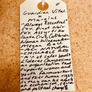 Handwritten tag on a cork board with text about a wine and an organization supporting women and youth.