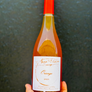 Bottle of orange wine with a red cap held against a dark background