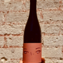 Wine bottle with decorative label featuring eyes and a mouth against a brick wall background