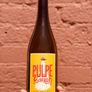 Bottle of Pulpe fashion with a yellow label against a brick wall.
