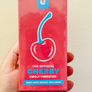 Hand holding a red packaging of 'The Official Cherry Emoji Vibrator' against a beige background