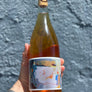 Hand holding a bottle of Rosé wine with a colorful label against a gray textured background