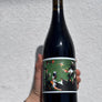 Wine bottle held by a hand with tattoos on a textured white background
