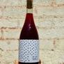 Bottle of red wine with a patterned label held against a textured wall.