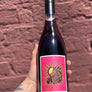 Wine bottle with a pink label featuring a zodiac design held against a brick wall.