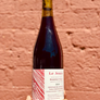 Bottle of red wine labeled 'Le Jeune' held against a brick wall.
