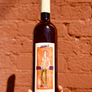 Bottle of 'Orange John Doe' wine held against a red brick wall.