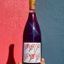 Bottle of red wine with a decorative label held against a red and blue wall.