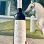 Wine bottle held in front of a decorative horse figure with a blurred background