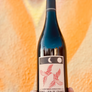 Wine bottle with a label featuring a bird design held against an abstract orange and yellow background.
