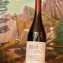 Bottle of Morgon wine held in front of a painted mural with animals and landscapes.