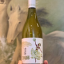 Bottle of white wine with a decorative label held in front of a horse painting.