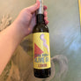 Hand holding a bottle of olive oil with a yellow label on a reflective surface.