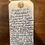 Handwritten tag on a wooden surface with text about a wine product.
