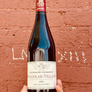 Bottle of Chateau de Lavernette Beaujolais-Villages 2021 held against a red brick wall.