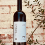 Bottle of Krya wine held in front of a textured wall with greenery.