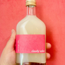 Bottle of 'cloudy sake' with a pink label held against a red background