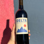 Bottle of Delta Cabernet Sauvignon wine held by a person against a blue and pink background