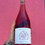 A hand holding a bottle of Kareen Barbera Rosato rosé wine against a bright pink textured wall. The bottle has a white label with a purple illustration of a fish and the brand name 'KAREEN' at the top.