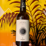A hand holds a bottle of Mirabés 2025 Barolo red wine. The bottle has a cream-colored label with black text and a circular graphic, topped with a red cap.