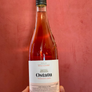 A hand holding a bottle of Ostatu Rosado 2020 rosé wine against a textured red background.