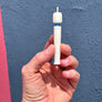 A hand holding a small white cylindrical object with a blue band and a white tip, set against a textured blue wall with a pink stripe at the bottom.