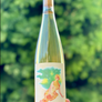 Wine bottle with a colorful label held against a blurred green background