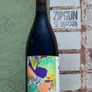 Bottle of wine with a colorful label held against a textured wall.