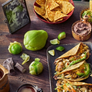 Plated tacos with tortilla chips, limes, and a cup of coffee on a wooden table.