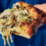 Hand holding a piece of cheesy bread with herbs against a blue background