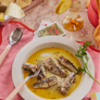Plate of fish in a yellow sauce with a fork on a pink tablecloth.