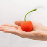 Hand holding a red cherry-shaped vibrator against a white background