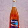 a hand holding a pink wine bottle with label that has a racecar on it against a blurry background
