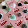 Pink cards with heart-shaped stones labeled 'you're a GEM!' on a wooden surface.