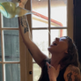 Person pouring a drink from a bottle into a glass with a window in the background