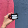 A hand holding a small black jar soy candle labeled 'VIVA LA VULVA' against a split pink and blue textured wall background.