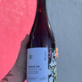 Hand holding a bottle labeled 'SKOG 03' against a pink and gray background