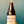 A hand holding a glass bottle of Pet-Nat Red wine against a teal painted wall. The bottle has a cream-colored label decorated with colorful birds and the brand name 'Mau Poma' visible at the top.