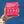 A hand with a floral tattoo holds a pink box of a dietary supplement against a solid blue background. The back of the box features white text and three circular botanical icons.