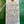 A handwritten wine tag on cream paper with a wooden grommet and white string, listing several Oay Wines, photographed against a textured green background.