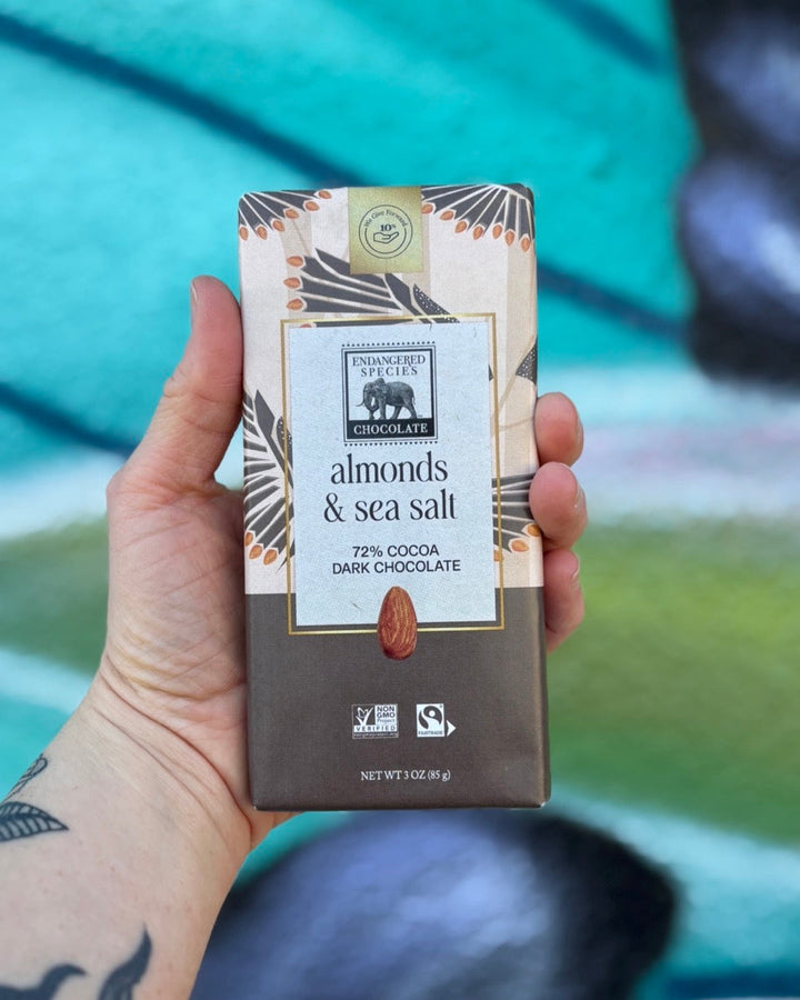 Hand holding a chocolate bar packaging with 'Almonds & Sea Salt' flavor against a blurred background