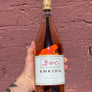 Bottle of Enkidu Rosé wine held against a textured red brick wall.